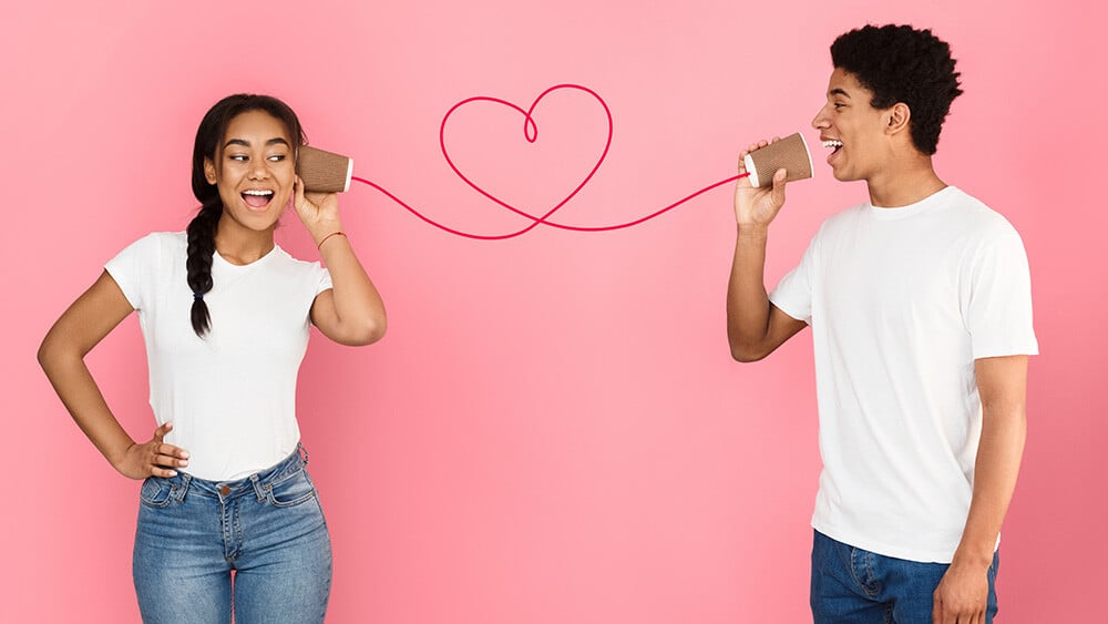 A young woman and man using a tin-can phone with a heart-shaped string, symbolizing clear communication through IVR-CRM integration.