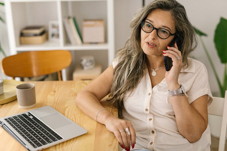 Woman speaking on the phone demonstrating the importance of emotional intelligence and active listening in customer service, with a laptop open on the table